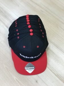 Das Bild zeigt eine Cap in den Farben Rot und Schwarz, die mit dem Logo von TopTech bestickt ist. Die Cap hat eine typische Baseball-Cap-Form mit einem vorgebogenen Schirm und einem verstellbaren Riemen am Hinterkopf. Die rote Farbe der Cap dominiert das Design, während das schwarze TopTech-Logo auf der Vorderseite gut sichtbar ist. Das Logo ist in weißer Farbe ausgeführt und hebt sich deutlich vom roten Hintergrund ab. Die Stickerei ist von hoher Qualität und verleiht der Cap eine professionelle und ansprechende Optik. Die Cap selbst ist aus hochwertigem Material gefertigt und bietet einen hohen Tragekomfort. Der vorgebogene Schirm schützt das Gesicht vor Sonnenlicht und die Belüftungslöcher auf der Oberseite der Cap sorgen für eine gute Luftzirkulation. Der verstellbare Riemen am Hinterkopf ermöglicht eine individuelle Anpassung der Cap an den Kopfumfang des Trägers. Die Cap ist ein ideales Werbegeschenk für Kunden und Mitarbeiter von TopTech. Sie eignet sich auch perfekt als Teil der Arbeitskleidung für das Personal des Unternehmens oder als Merchandise-Produkt für Fans der Marke.