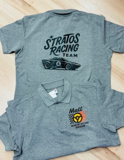 Zwei graue T-Shirts auf Holz, bedruckt mit Rennwagen-Motiv und Firmenlogo, ideal für Vereins- oder Firmenbekleidung in der Schweiz.
