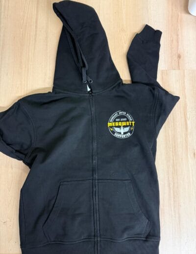 Schwarze Kapuzenjacke mit Reissverschluss, Textildruck-Logo "MEGAWATT" vorn, geeignet für Firmen- oder Vereinsbekleidung.